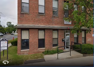 Brick two-story building exterior with a sidewalk, ramp, and a front sign.