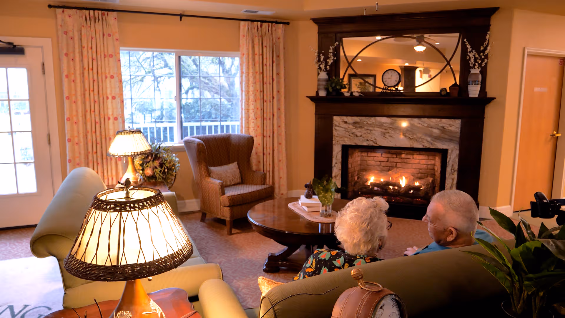 Cozy living room at Terpening Terrace with a lit fireplace, sofas, and two residents seated.