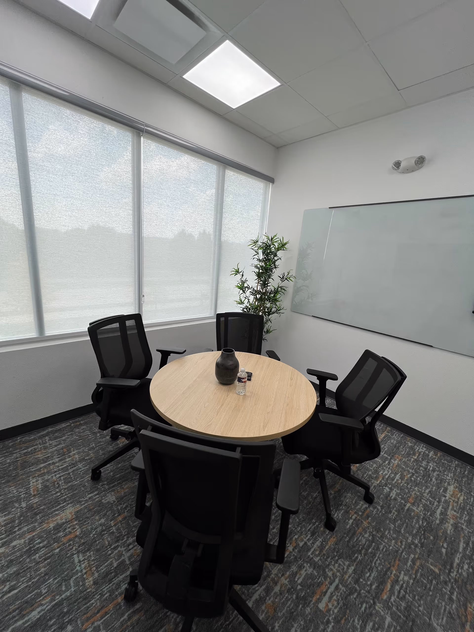 Round wooden table with five black chairs in a bright meeting room.