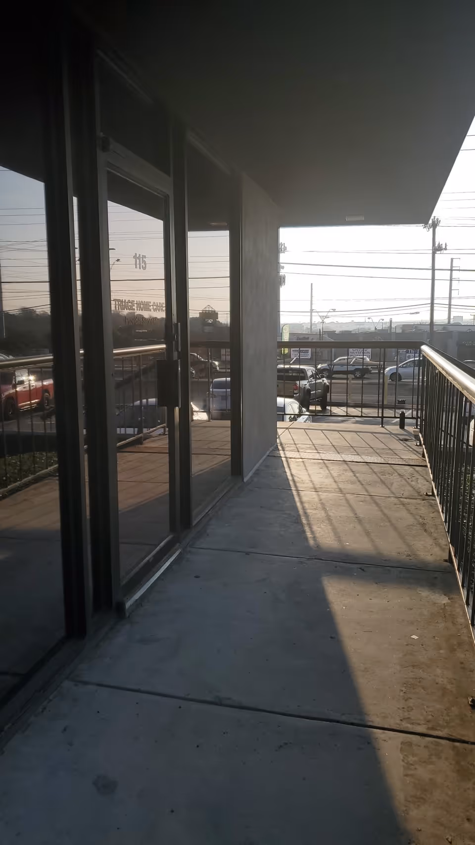 Exterior walkway of Triage Home Care facility with glass doors and railing overlooking a parking lot.
