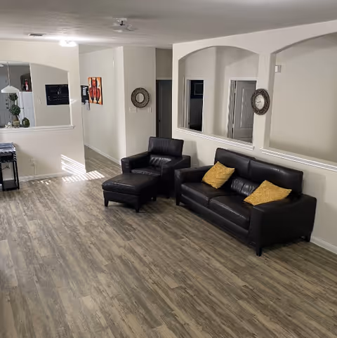 Modern lounge area with black leather sofas, an ottoman, and wall mirrors.