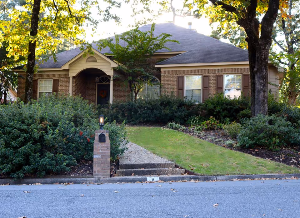 Brick, single-story home with a manicured lawn, walkway, and surrounding shrubs