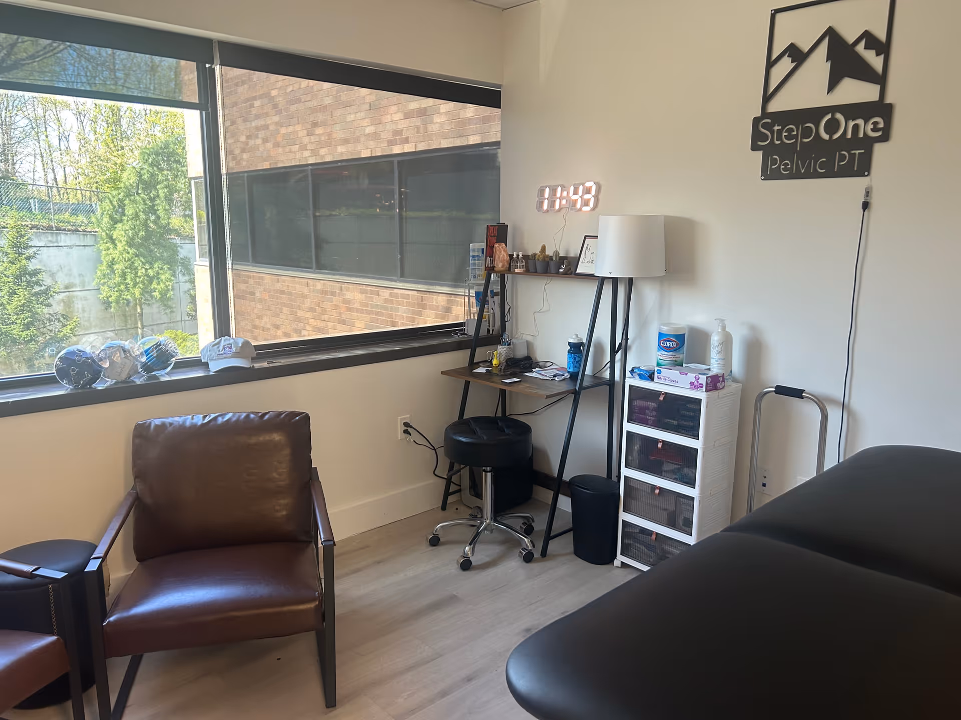 Interior therapy room with a treatment table, desk, storage, and Step One Pelvic PT sign.