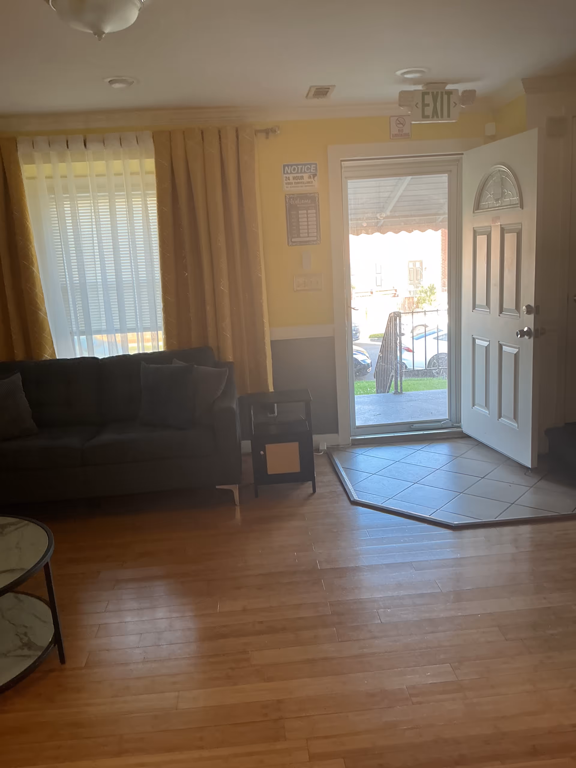 Living room area with sofa, curtains, small table, and open door to outside.
