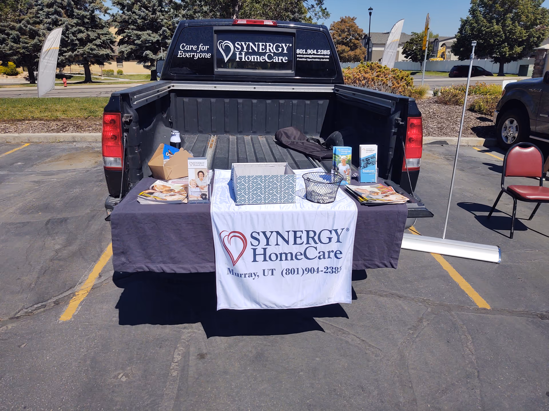 Promotional table with SYNERGY HomeCare banner in a parking lot.
