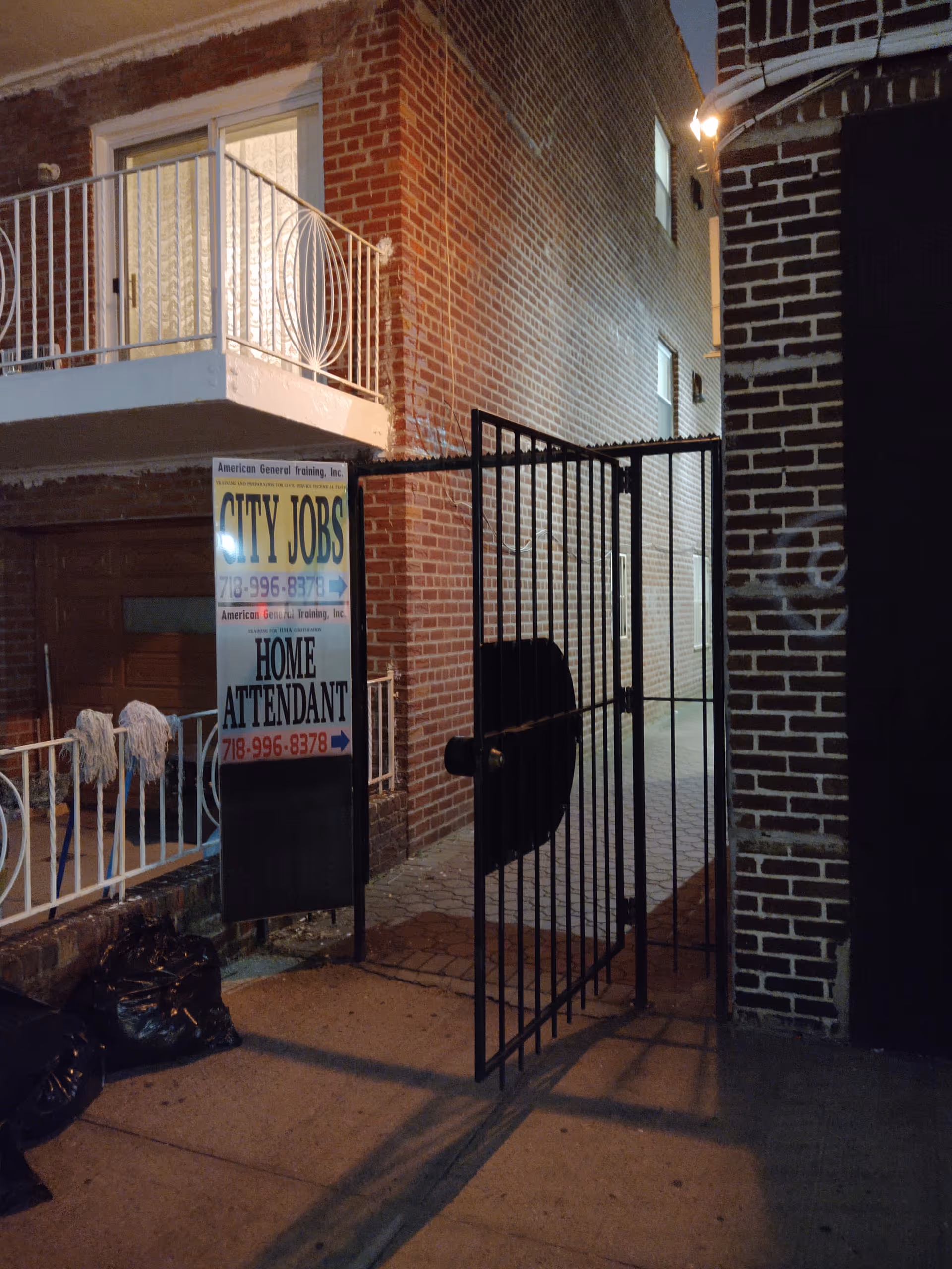 Night exterior of brick building with a metal gate and a sign advertising home attendants.