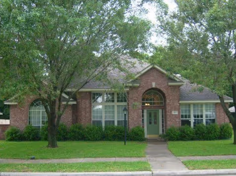 Brick senior living facility with a green front door, arched windows, and trees.