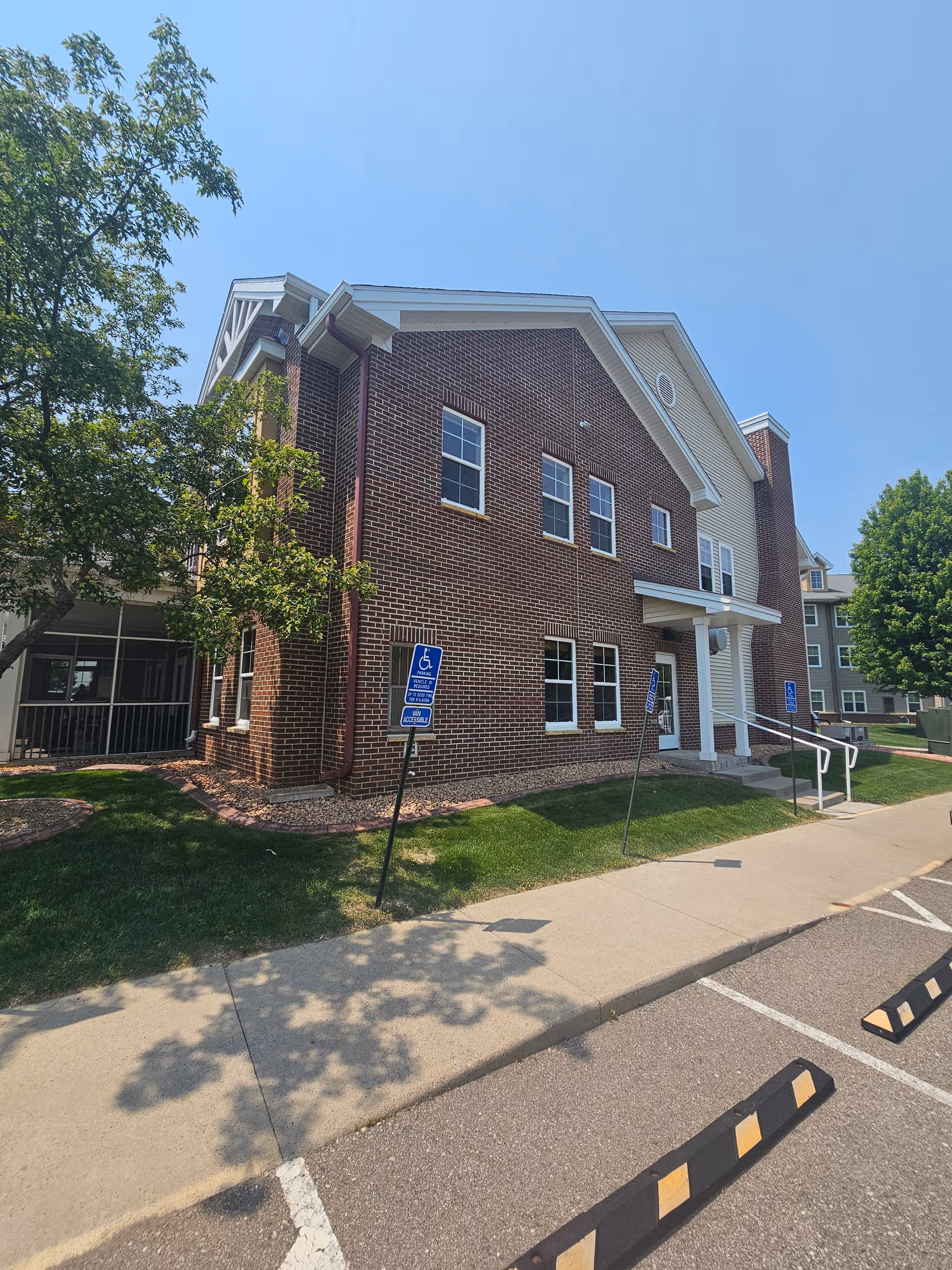 Brick senior living facility exterior with ramp, parking, and wheelchair-accessible signs near the entrance.