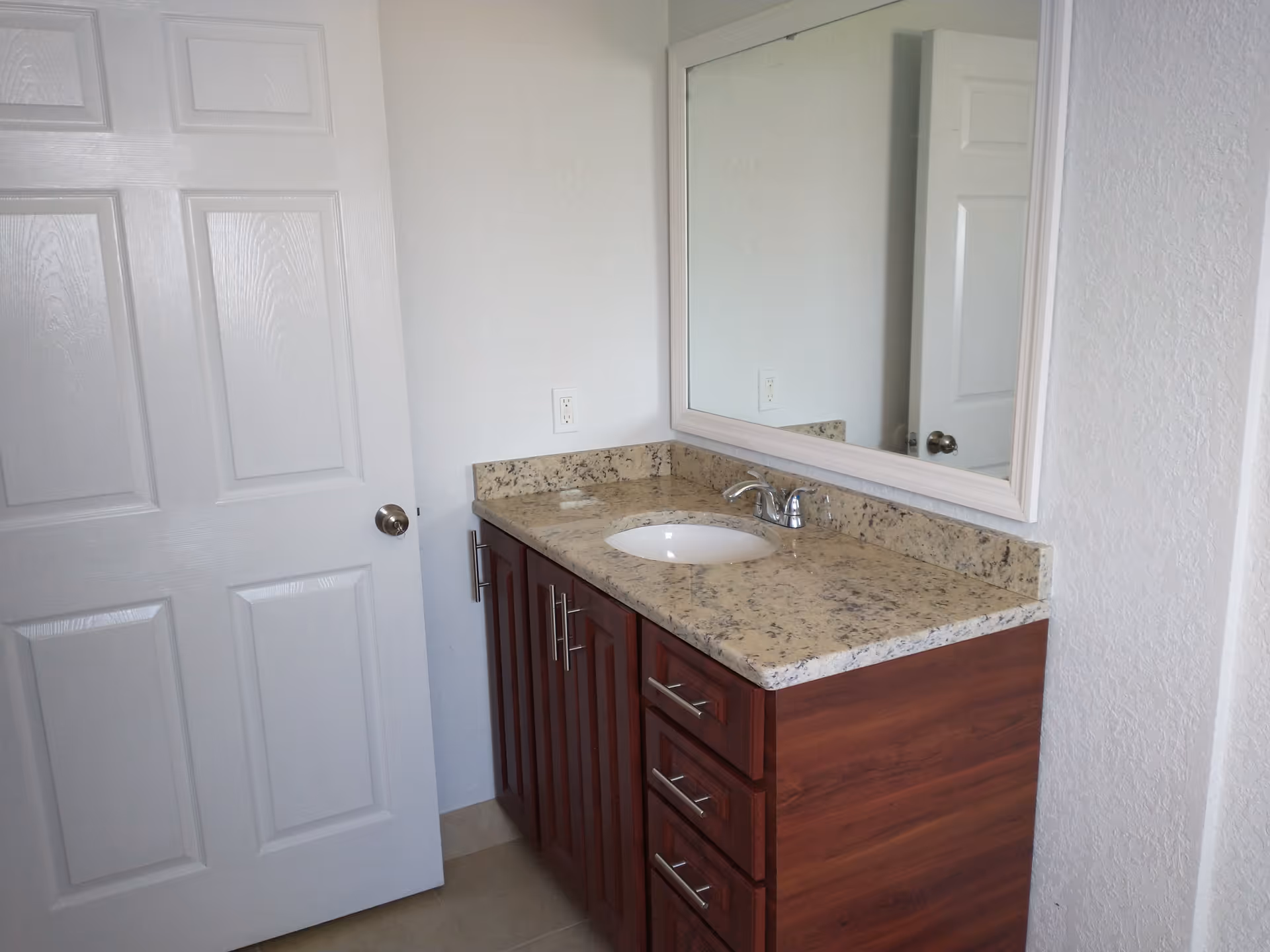 A bathroom vanity with granite countertop, sink, mirror, and wooden cabinets.