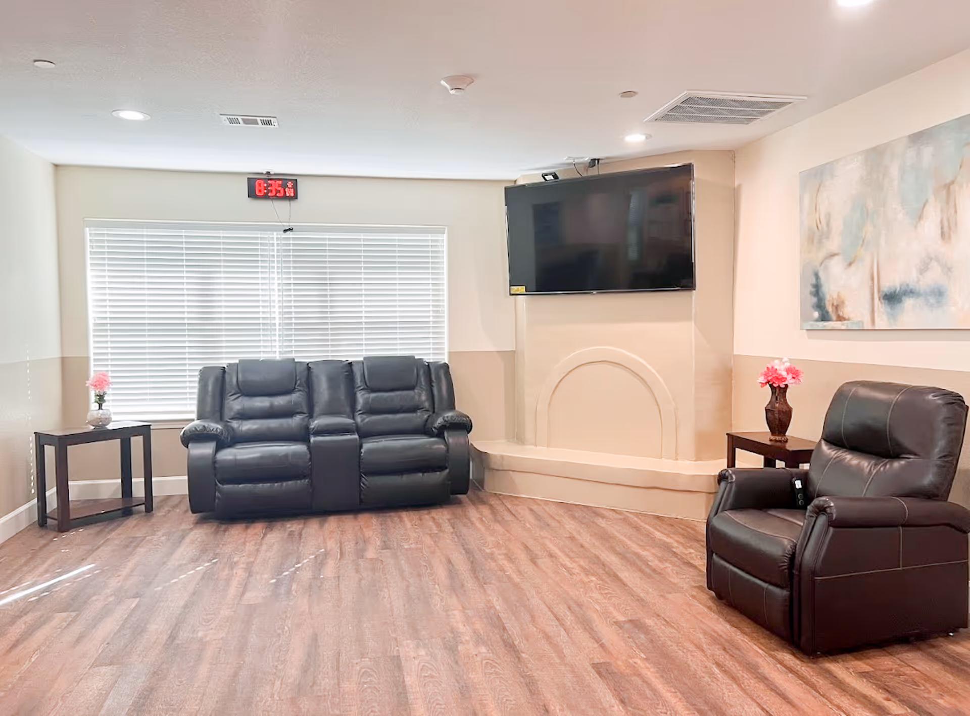 A cozy senior living lounge with black leather seating, TV, and side tables.
