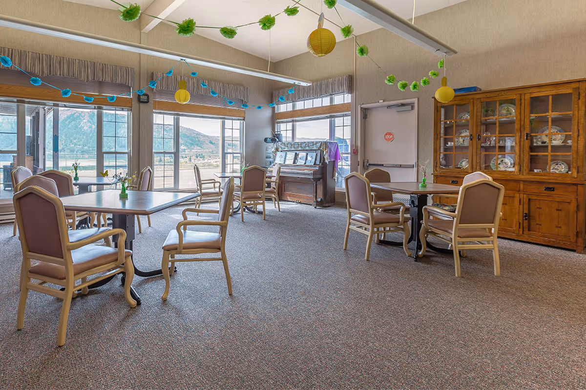 Sunlit dining area with tables, chairs, a wooden cabinet, and festive ceiling decorations.