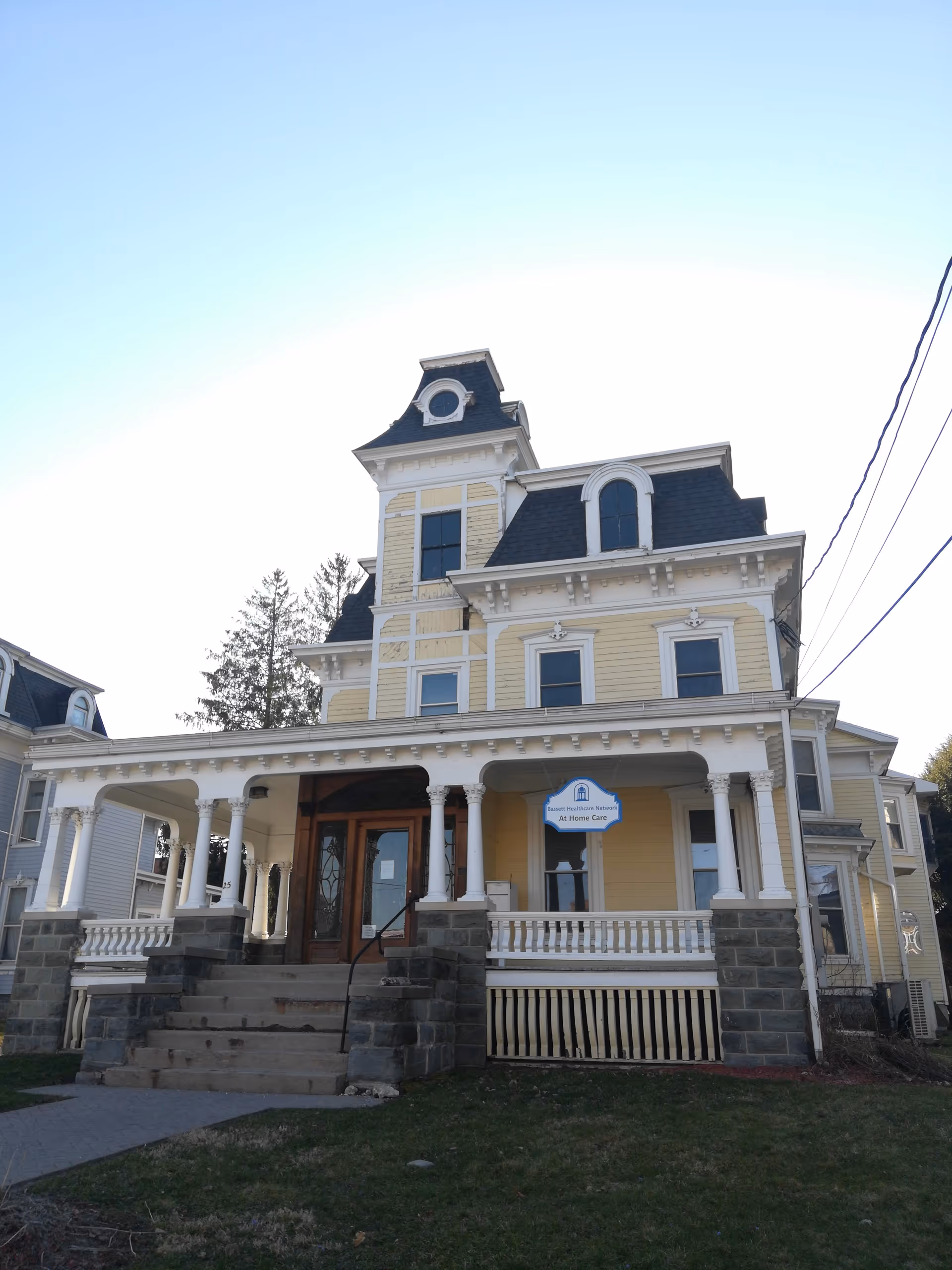 Yellow Victorian-style building with a wrap porch and steps, labeled At Home Care.