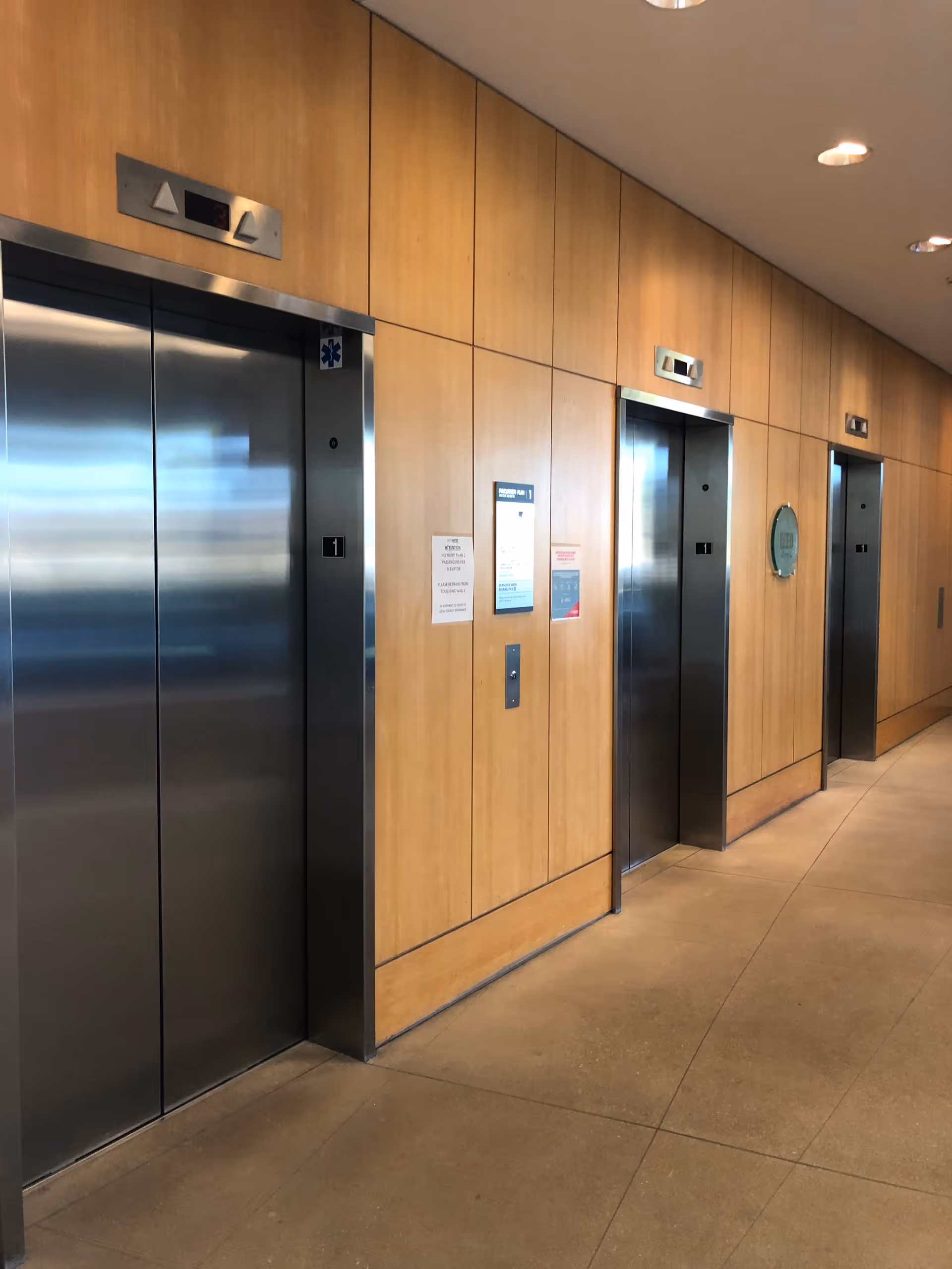 Interior hallway with wood-paneled walls and elevator doors along a tiled floor.