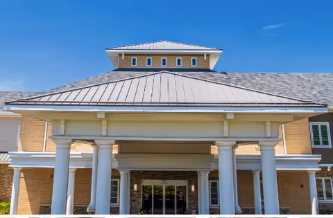 Front entrance of a brick senior living facility with white columns and blue sky.
