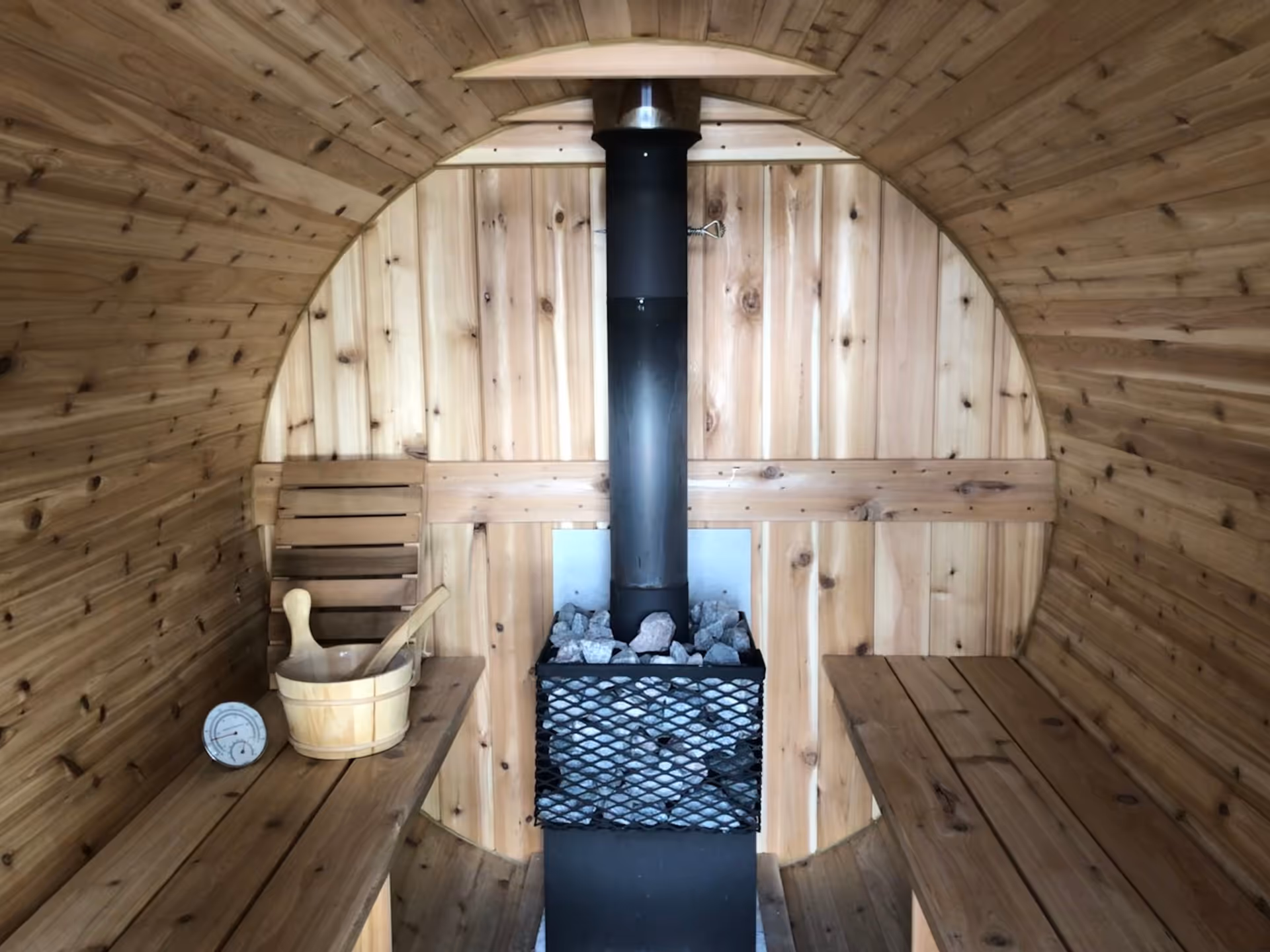Wood-paneled sauna interior featuring benches and a central stove.