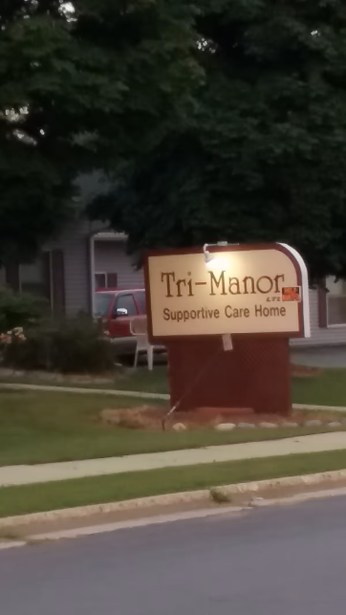 Tri-Manor supportive care home sign in front yard with trees and sidewalk
