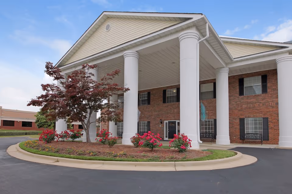 Brick senior living facility entrance with white columns and circular driveway.