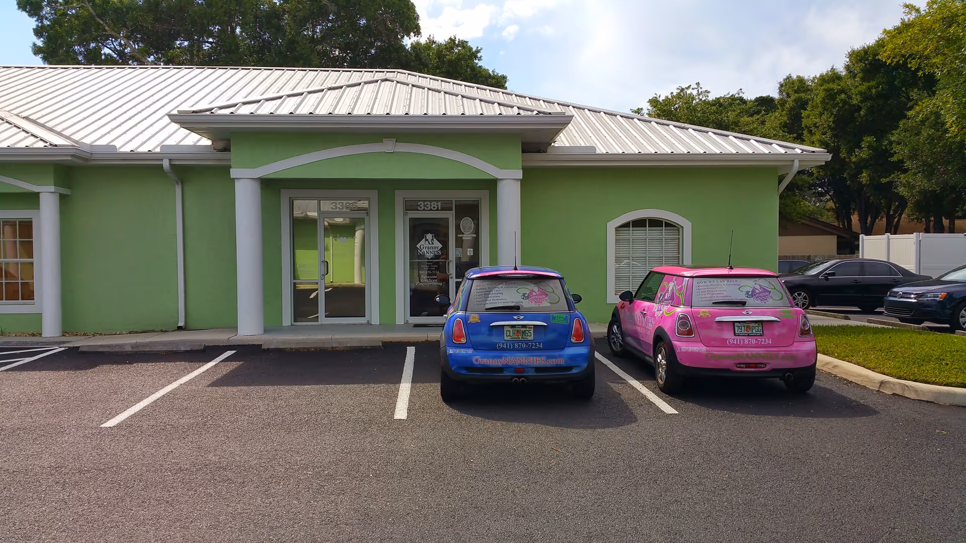Green, single-story building with a white roof and two parked colorful cars in front.