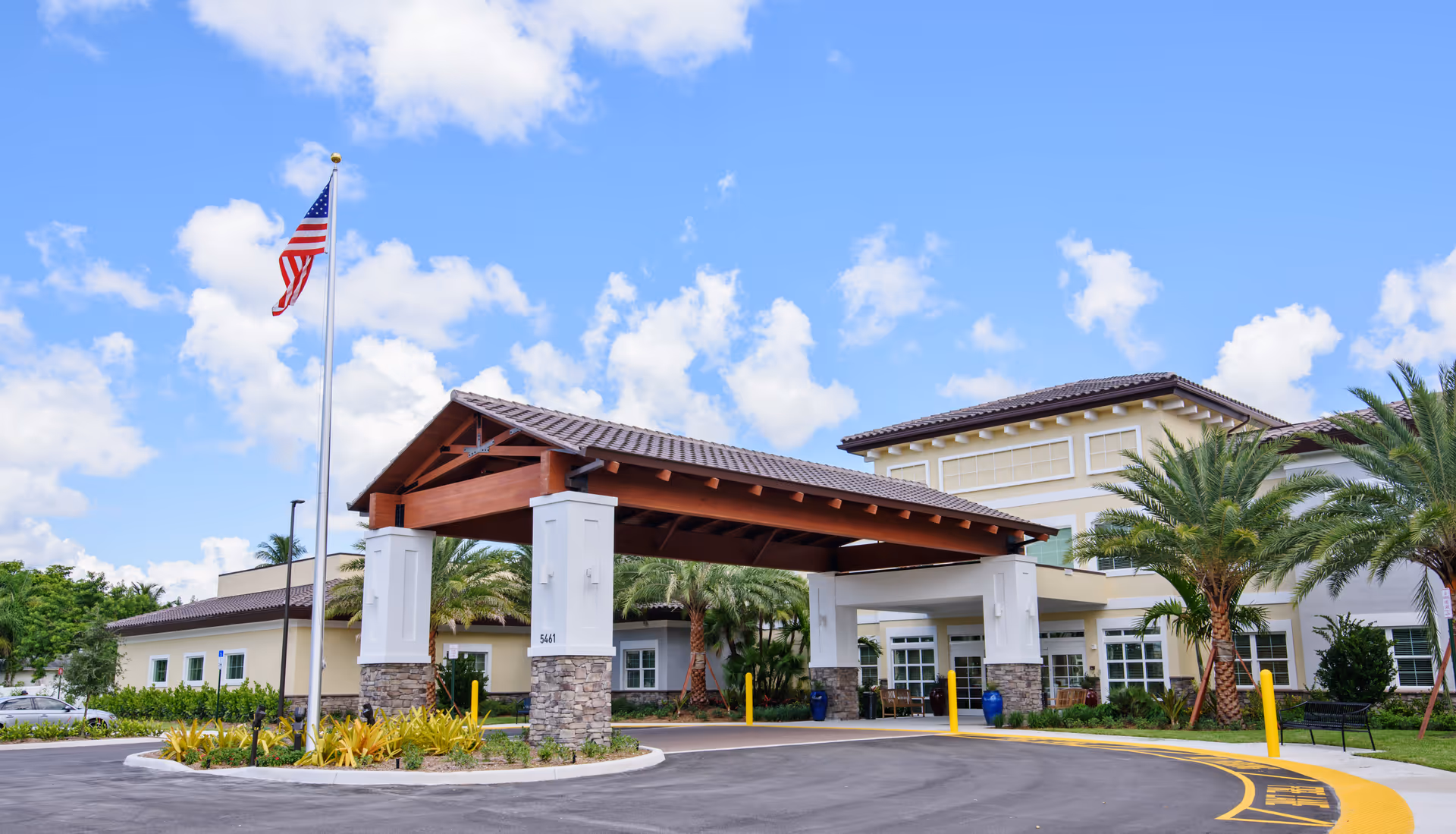 Exterior view of YOURLife of Coconut Creek facility with flag, palms, and a covered entrance.