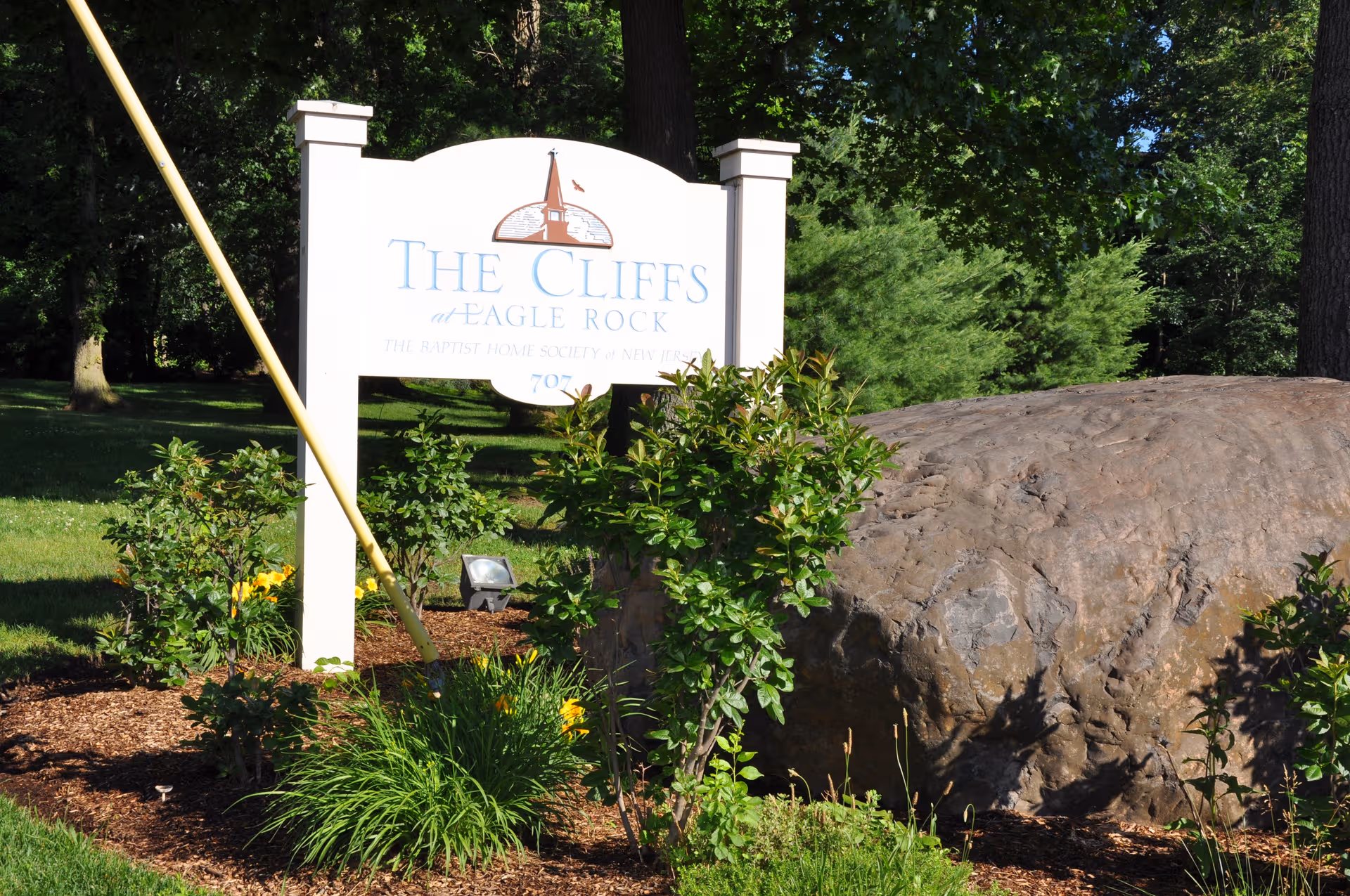 White sign reading The Cliffs at Eagle Rock stands beside a large rock with greenery.
