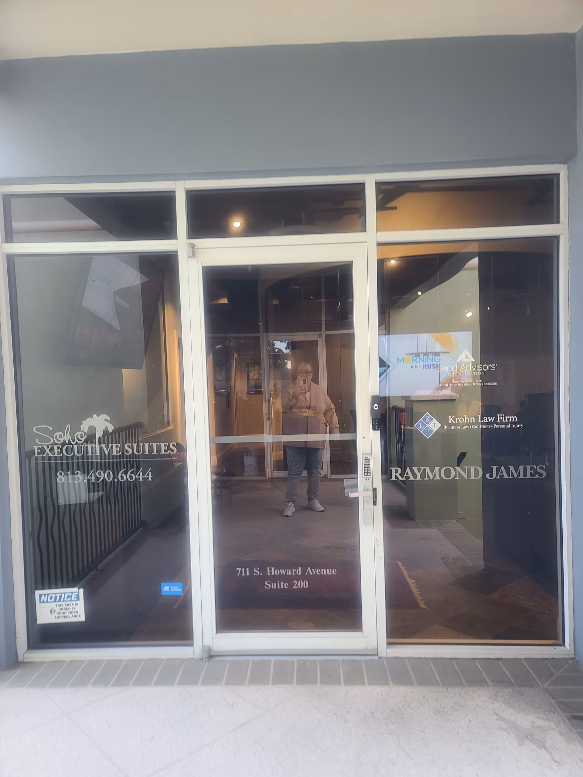 Glass storefront entrance displaying office logos; reflection of a person in the glass.