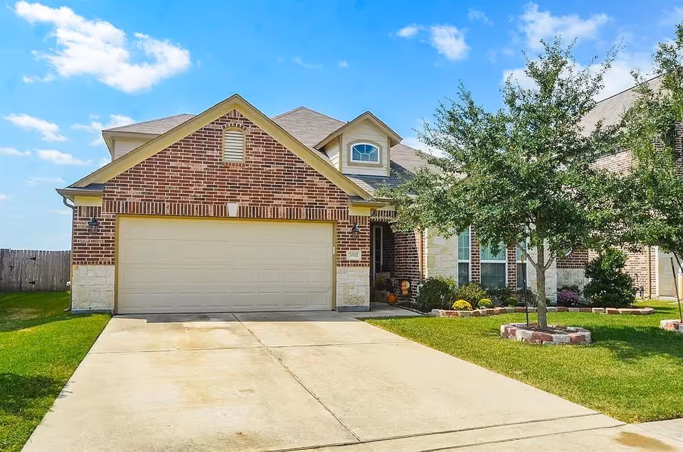 Brick house with a two-car garage, manicured lawn, and a tree in the front yard.