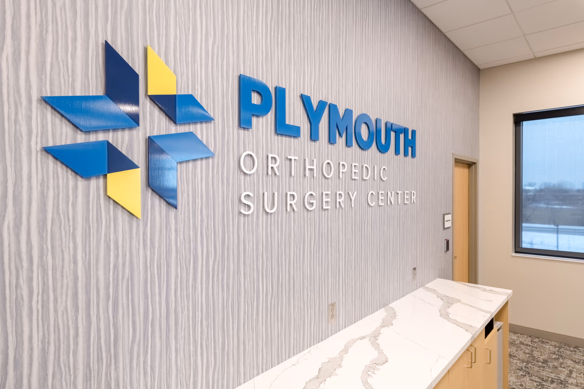 Interior reception area with Plymouth Orthopedic Surgery Center sign on textured wall.