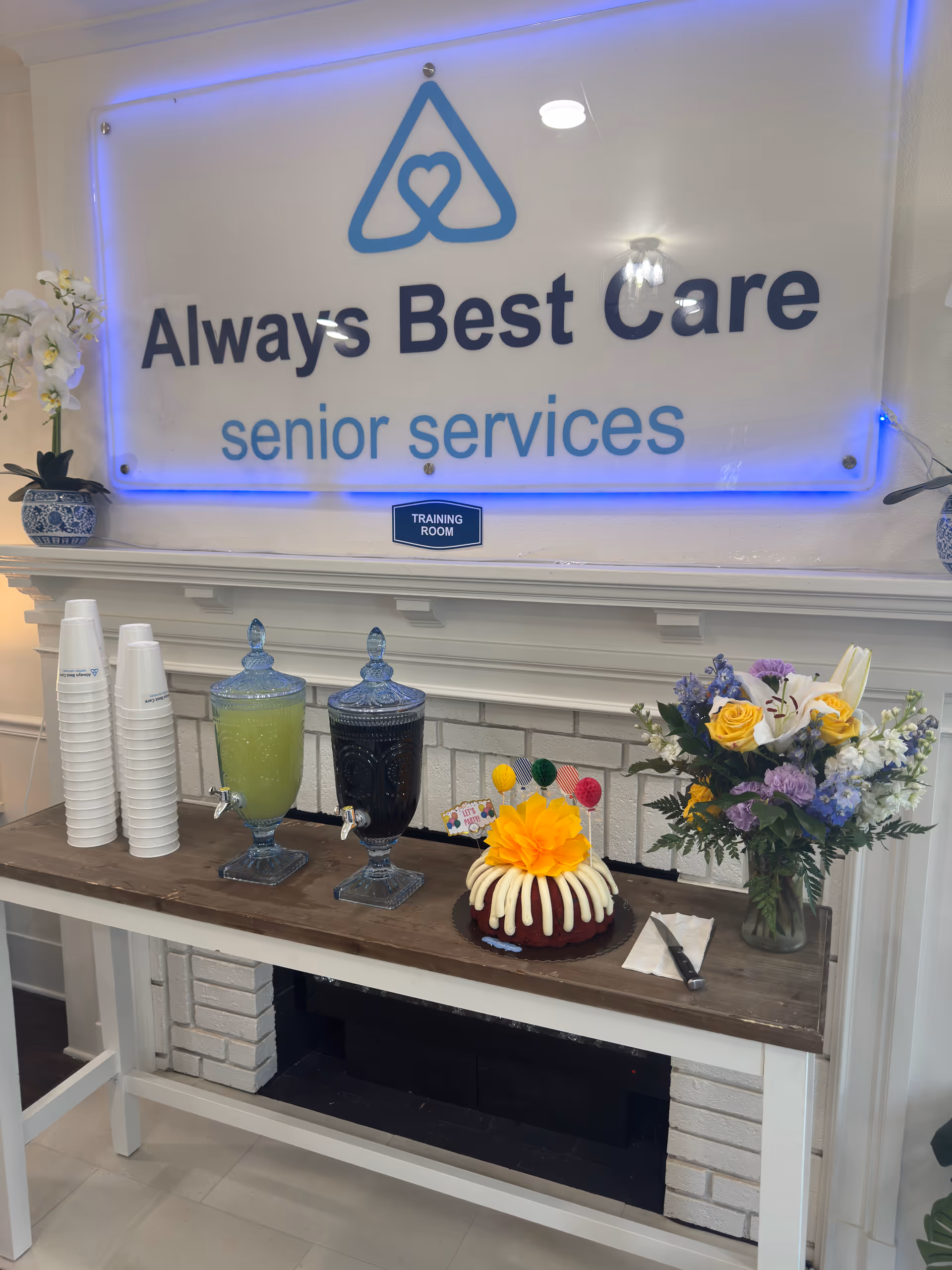 Interior reception area featuring Always Best Care sign, beverage station, cake, and flower arrangement.