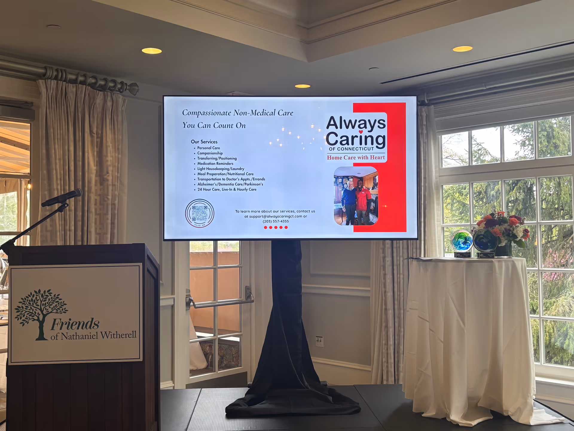 Interior presentation setup at a senior living facility with a large screen, podium, and floral table.