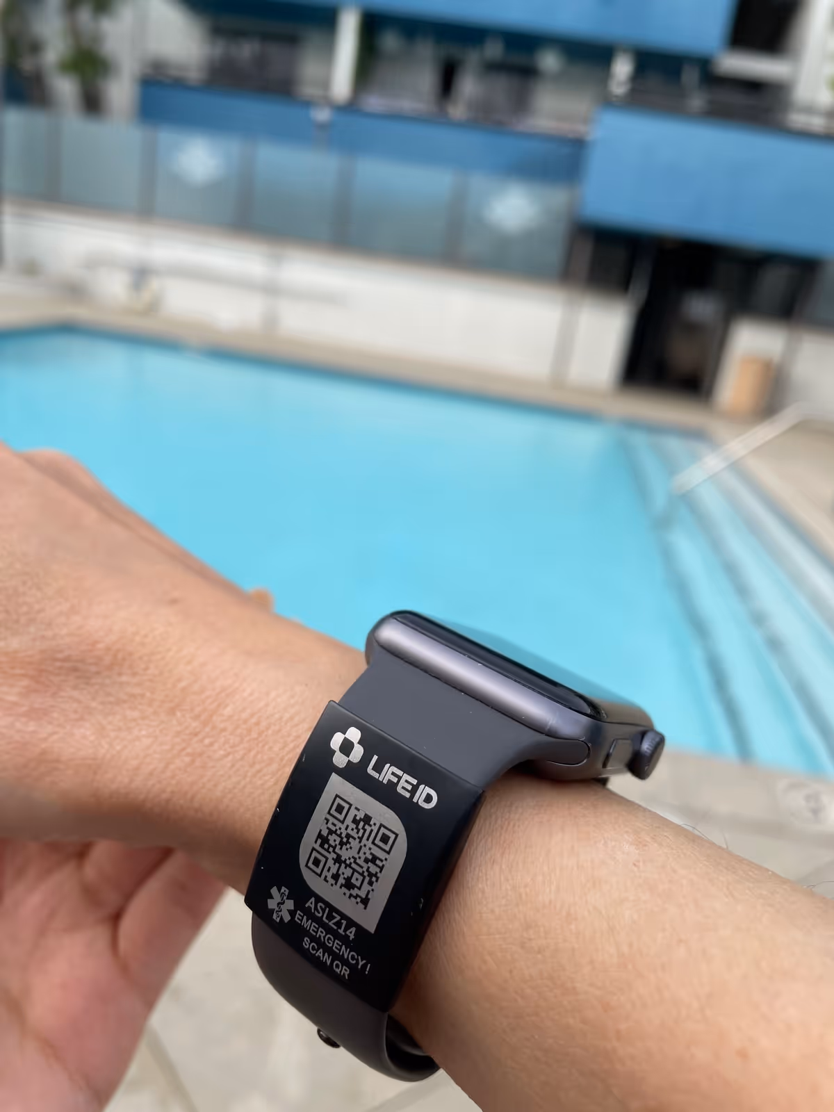 Close-up of LifeID wristband on wrist with outdoor pool in background.