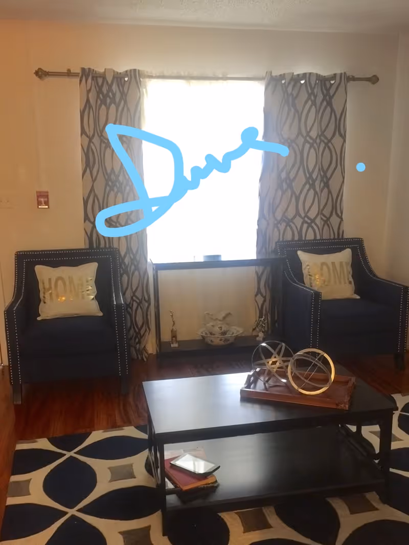 Cozy living room with two dark armchairs, a coffee table, and patterned curtains.