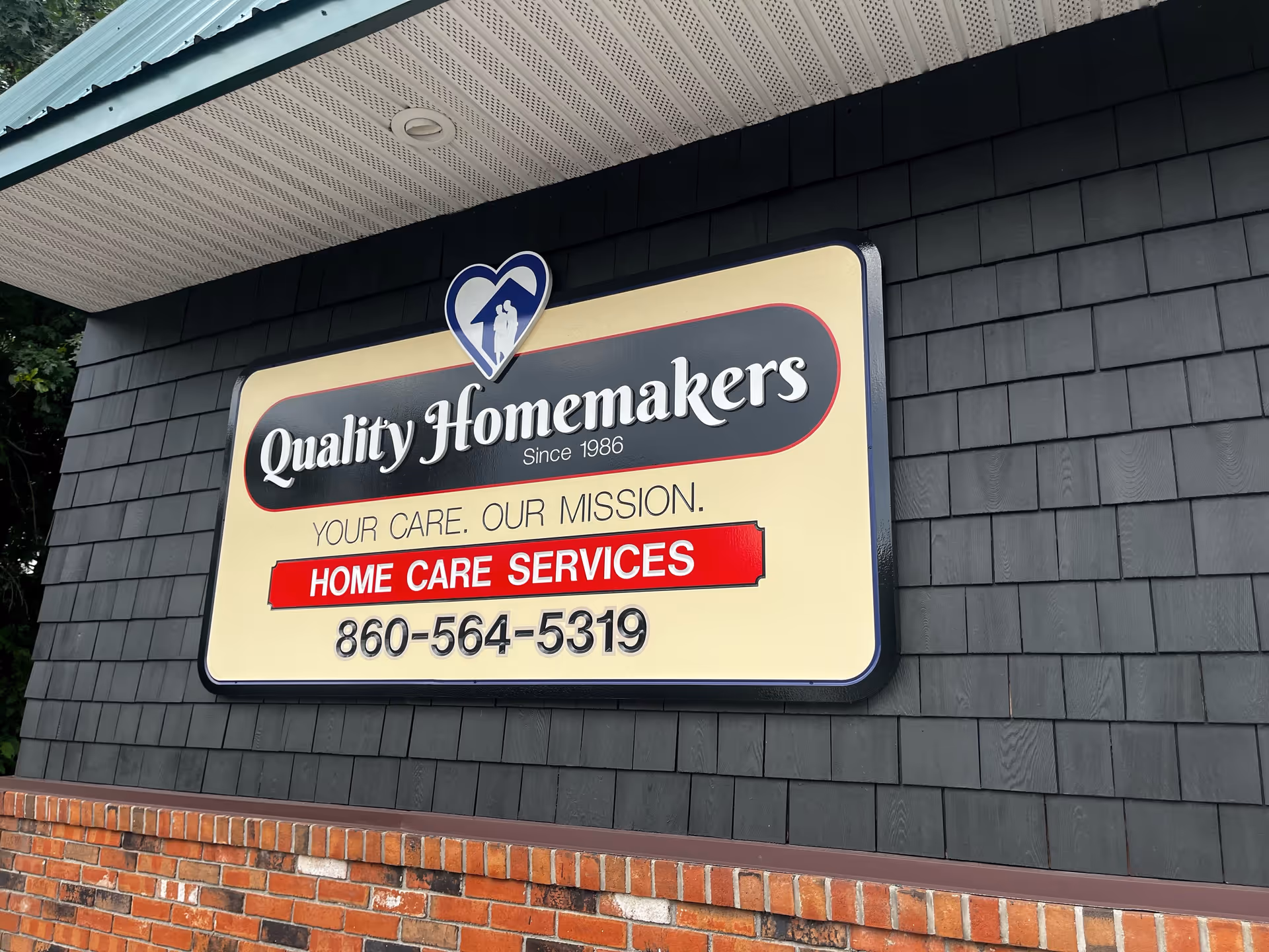 Exterior wall with a large Quality Homemakers sign advertising home care services and contact number.