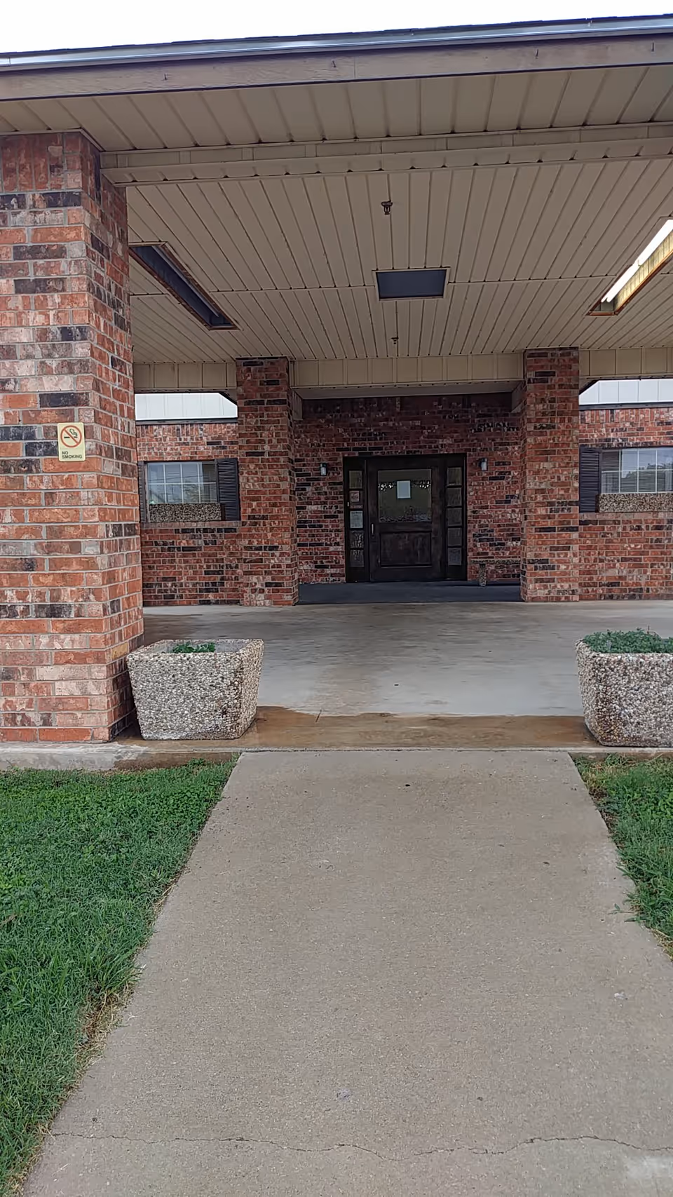 Brick facility entrance with a covered drop-off and concrete walkway.