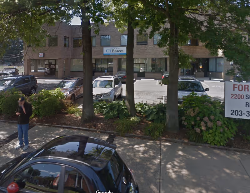 Exterior view of a brick building front with parked cars and trees.