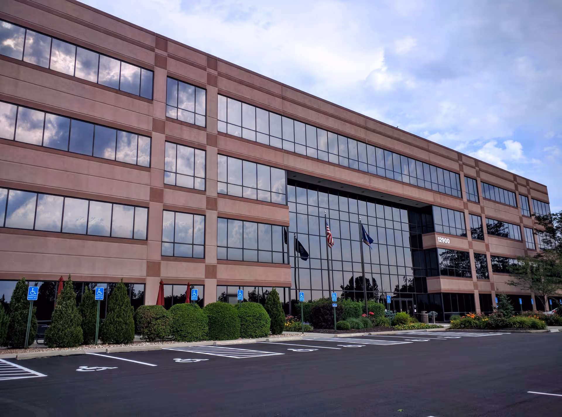 A modern brick building with a glass entrance, flags, and a large parking lot.