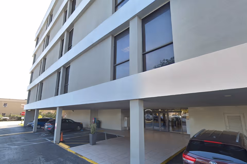 Exterior view of a multi-story senior living facility with a front entrance and parked cars.