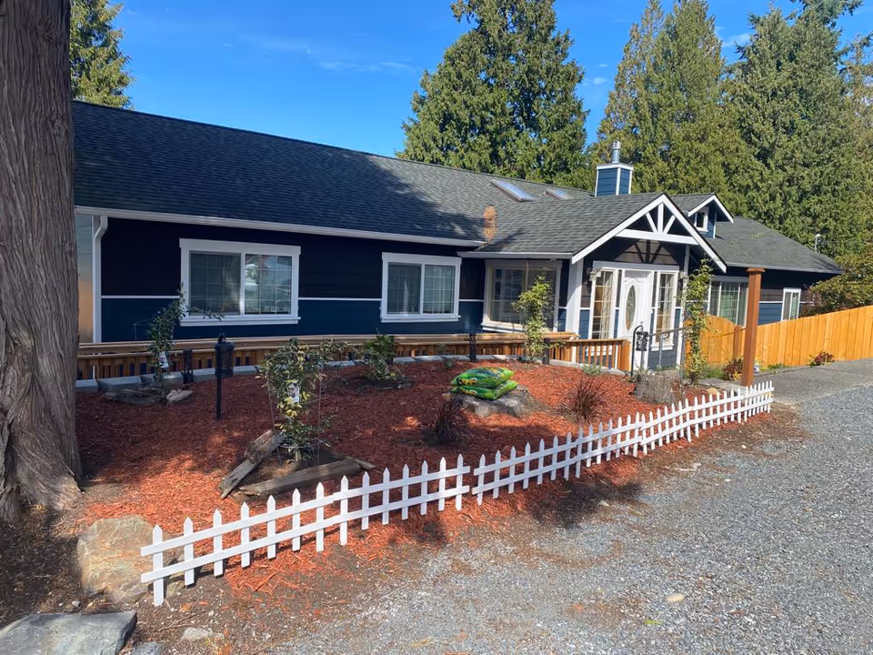 Blue single-story home with white trim, front yard landscaping, and a white picket fence.