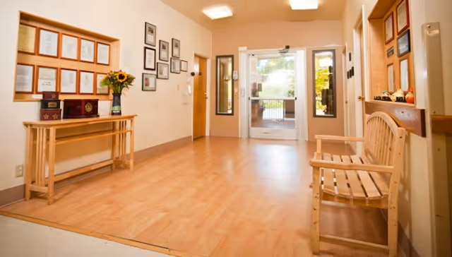 Bright reception/entry hall with a wooden bench and table, framed certificates on the walls, and glass double doors leading outside.
