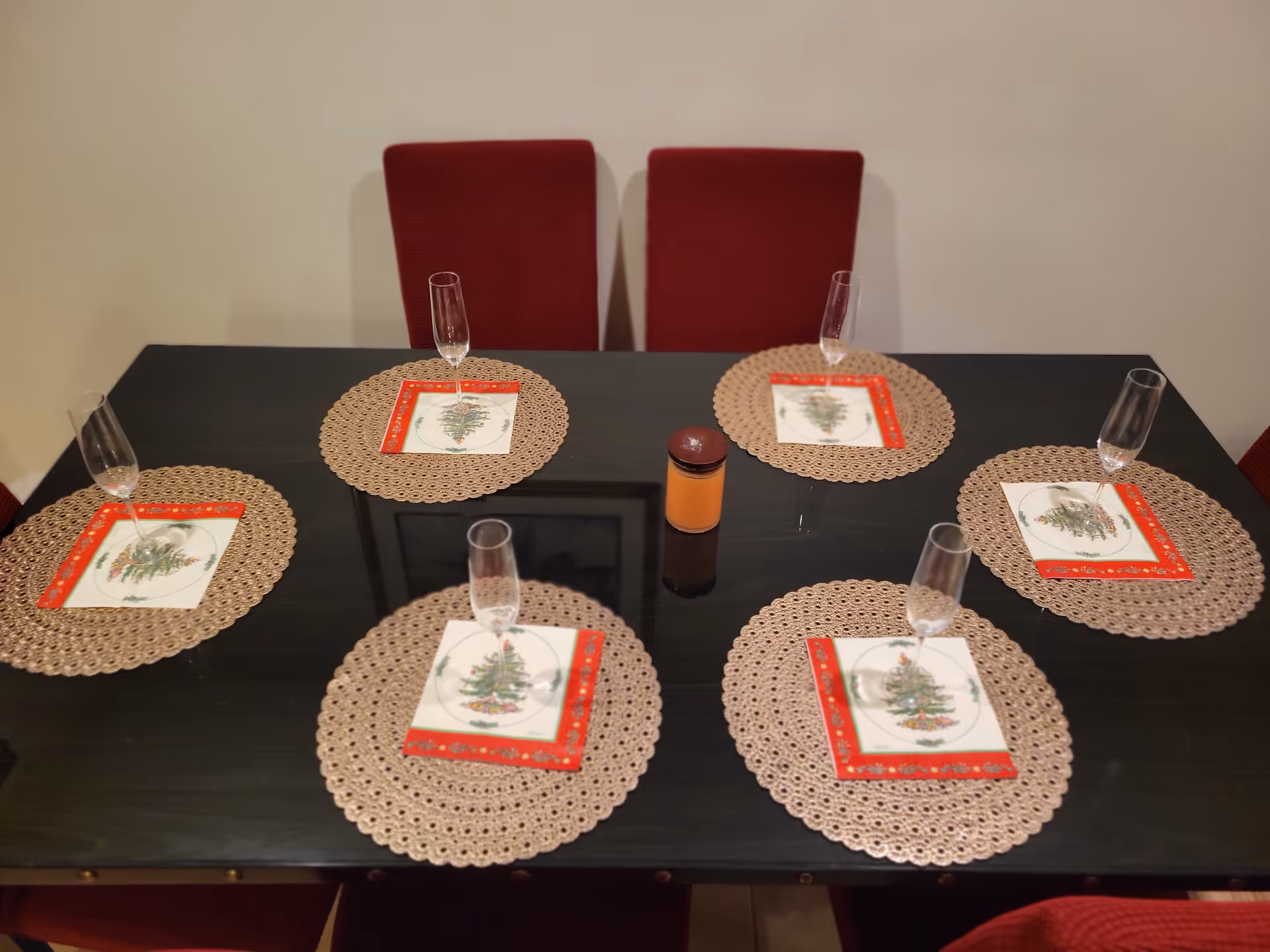 A dark dining table with six placemats, Christmas-themed napkins, and champagne glasses.