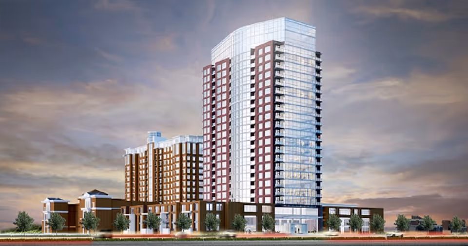 A modern multi-story senior living facility with a tall glass and brick tower and several lower connected buildings, set against a cloudy sky at dusk.