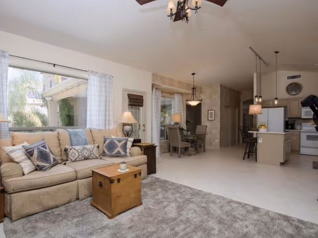 Open-concept living area with beige sofa, dining table, and kitchen in a bright, airy space.