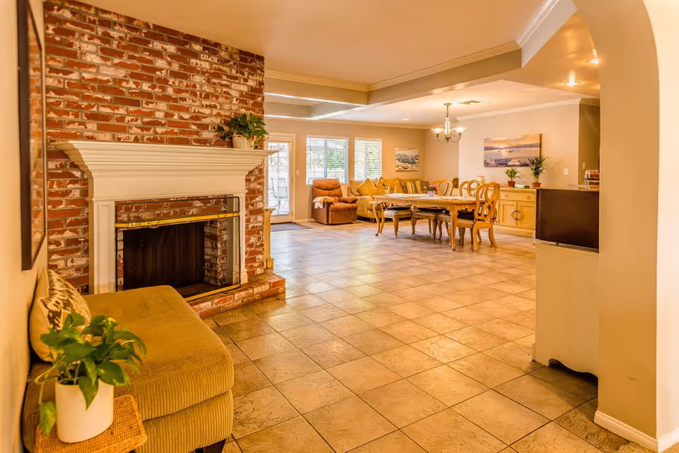 Open living and dining area with a brick fireplace, tiled floor, seating and a dining table.