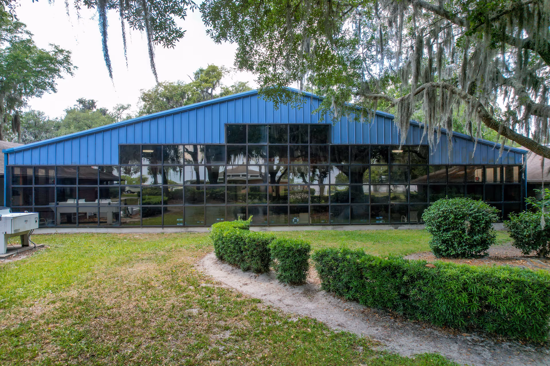 Low one-story blue building with large reflective windows facing a grassy yard and oak trees draped with Spanish moss.