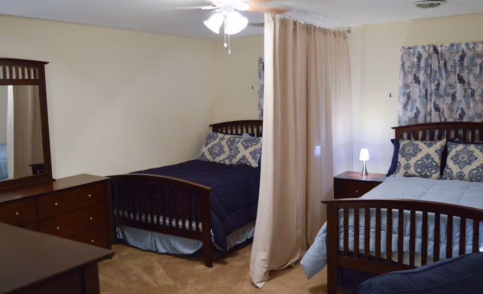 Two twin beds with a curtain divider in a beige, well-lit bedroom.