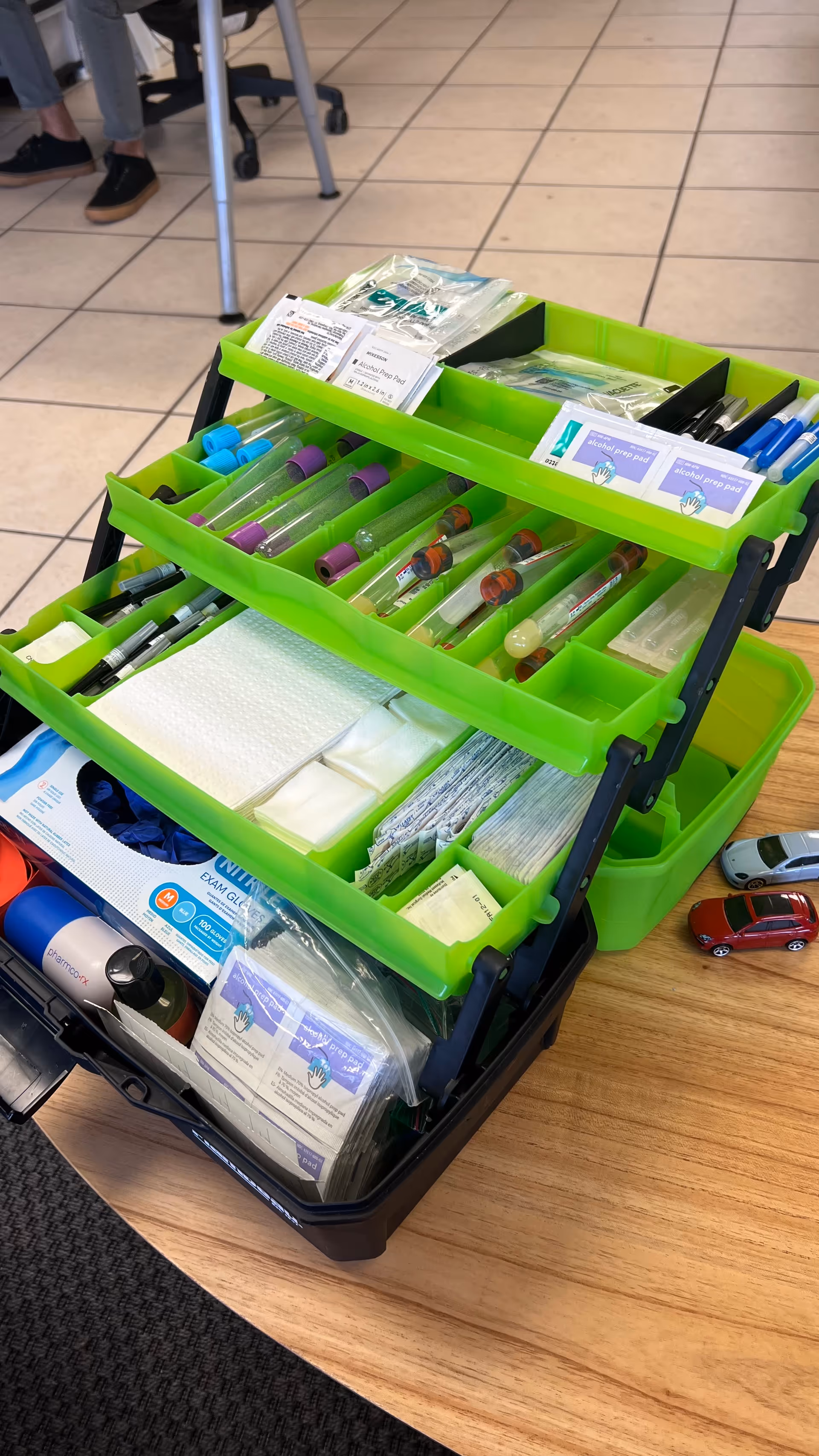 Bright green multi-tier medical supply cart with syringes and gloves indoors.