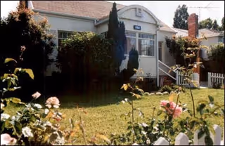 Front exterior of Burlingame Senior Home with a white building, porch steps, and rose garden.
