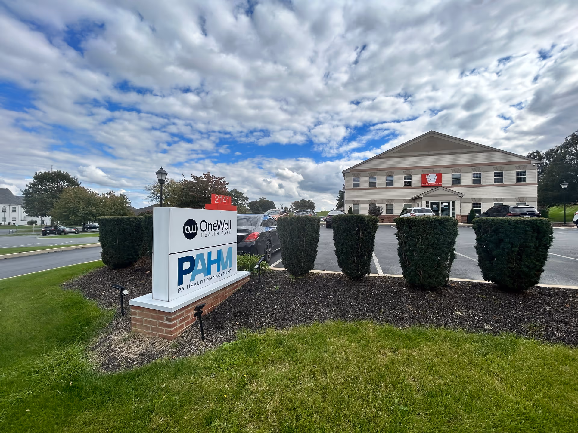 Front exterior of OneWell Health Care building with sign and parked cars.