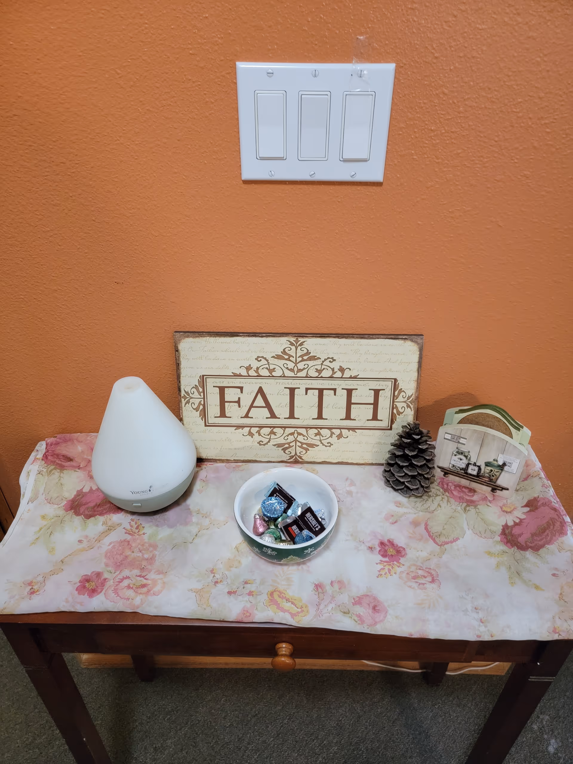 Orange wall with a light switch, table decor showing a 'FAITH' sign and diffuser.