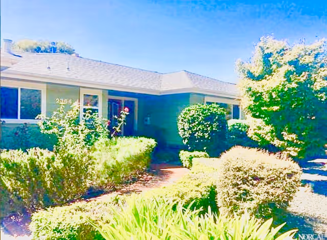 Single-story senior living facility exterior with manicured hedges along the entrance path.