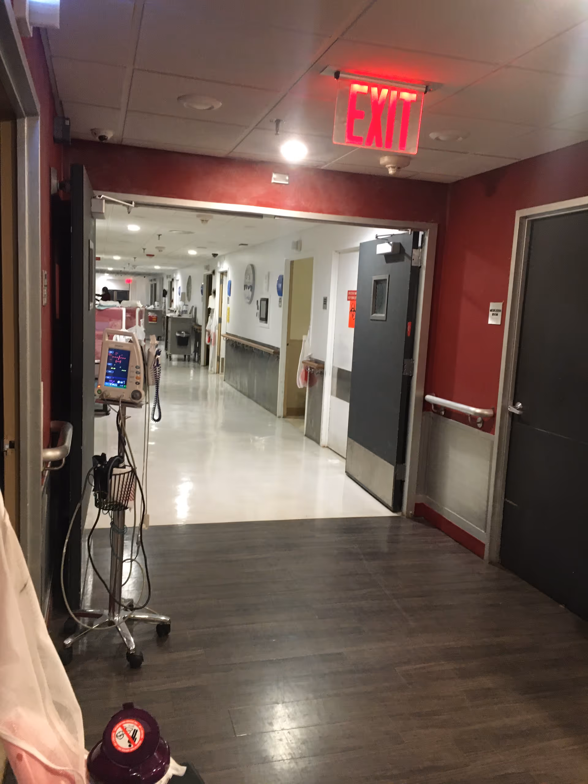 Interior hospital corridor with a medical cart and exit sign overhead.